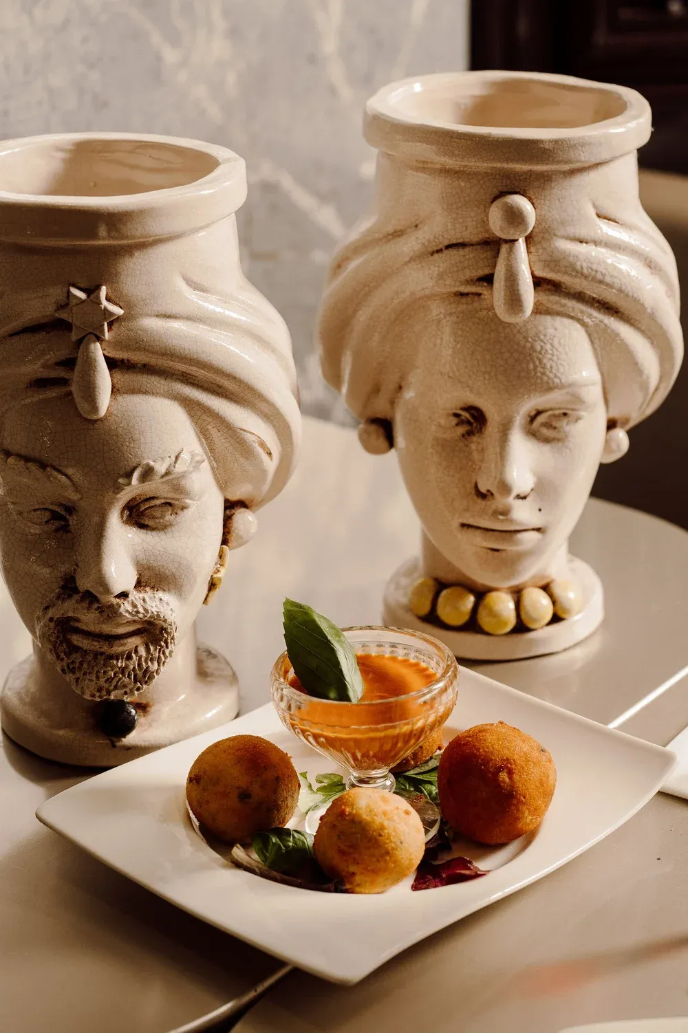 Arancini with a tomato dip, plated beside two Sicilian teste di moro ceramic vases