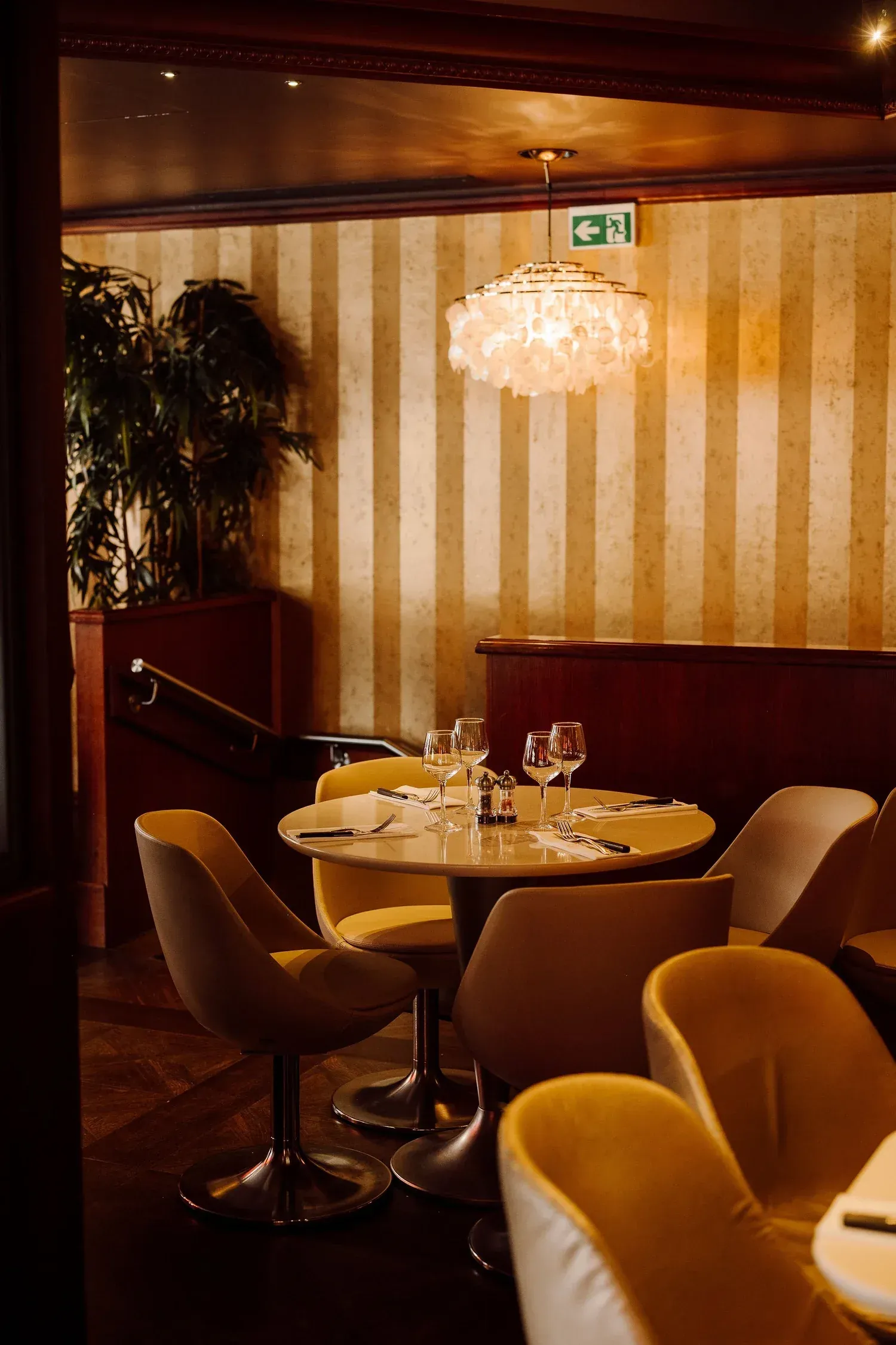 Dining room at Gran Caffè Convivium with a mother-of-pearl chandelier, striped walls and mustard velvet armchairs
