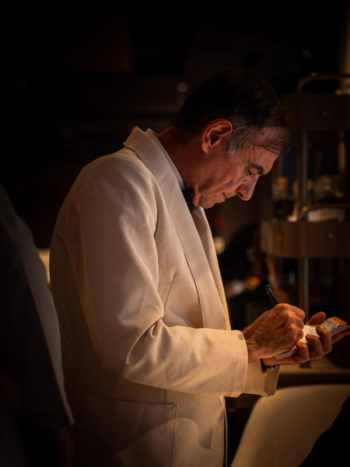 Maître d' in a white dinner jacket writing down an order in the dining room