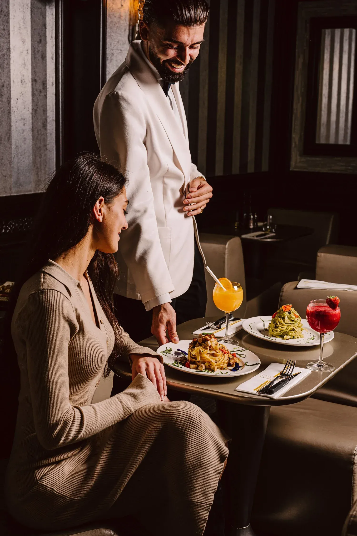 Waiter in a white jacket serving tagliatelle and cocktails to a guest
