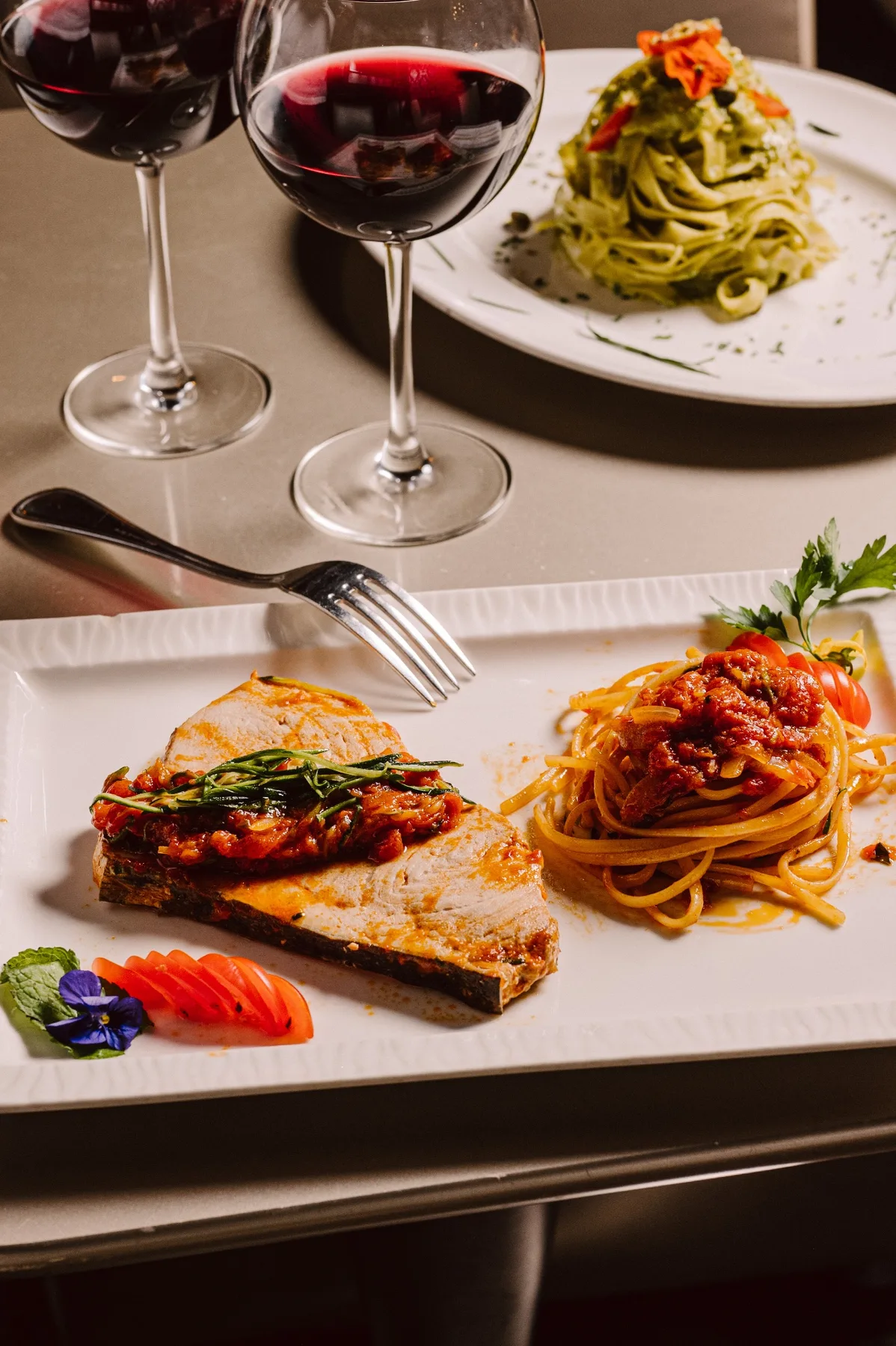 Espadon, linguine à la tomate et tagliatelle au pesto, verres de vin rouge